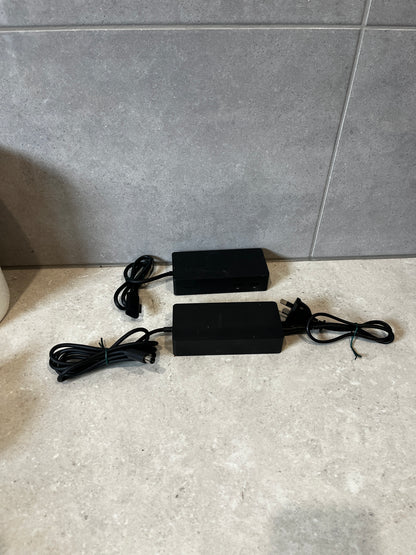 Two Microsoft Surface power adapters with cords on a stone surface
