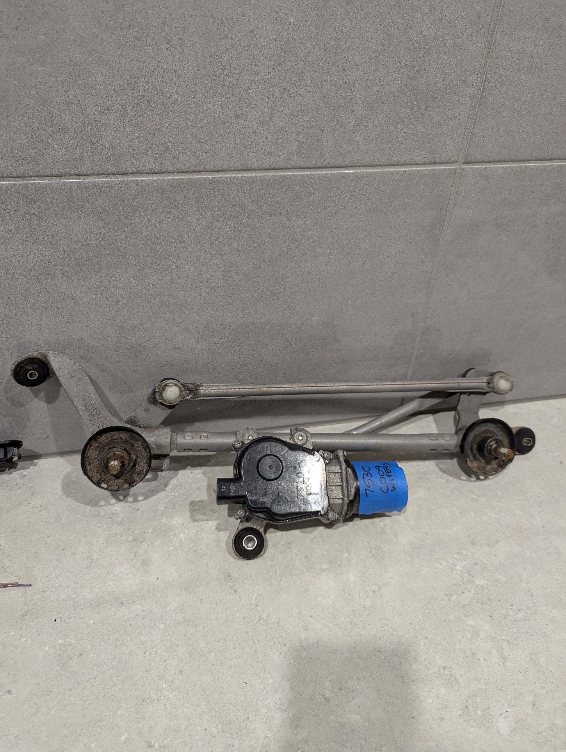 Full view of automotive wiper linkage and motor assembly on a gray surface