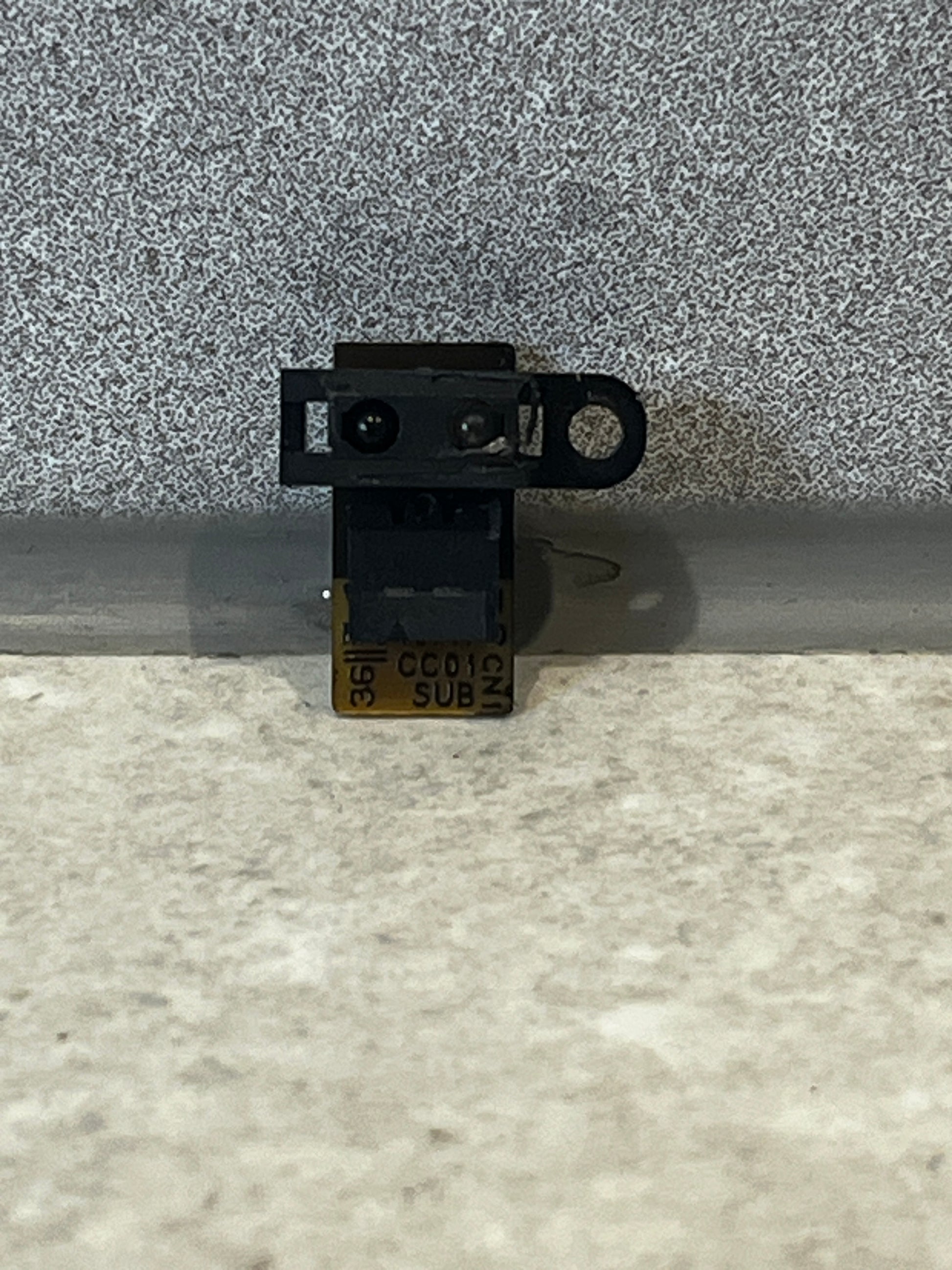 Close-up of a small black infrared camera module with a flexible circuit board for laptops