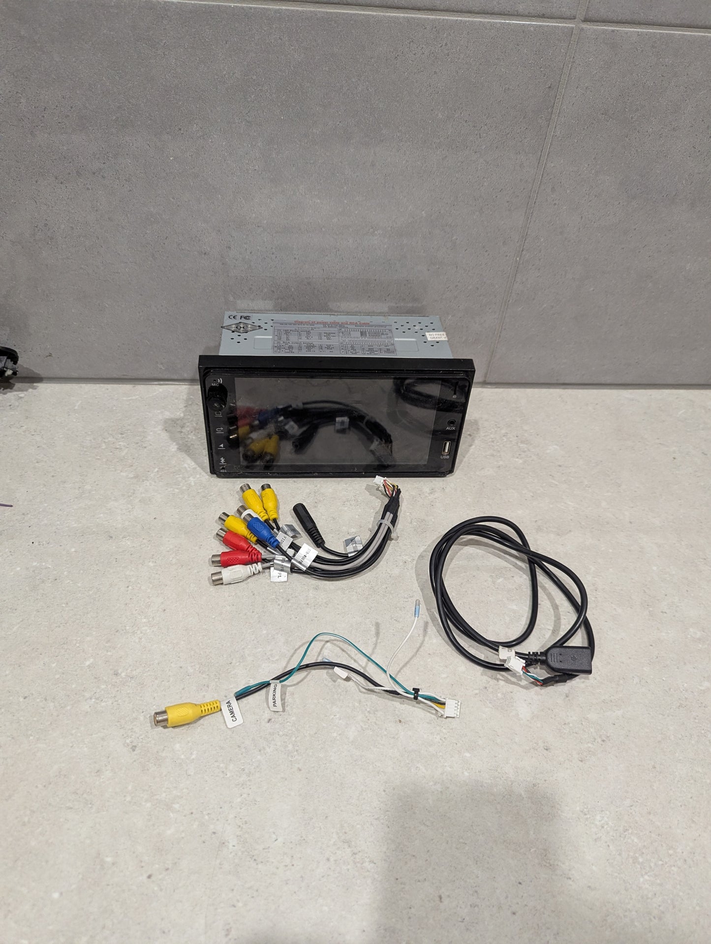 Double DIN car stereo head unit with wiring harness and RCA cables on a gray surface