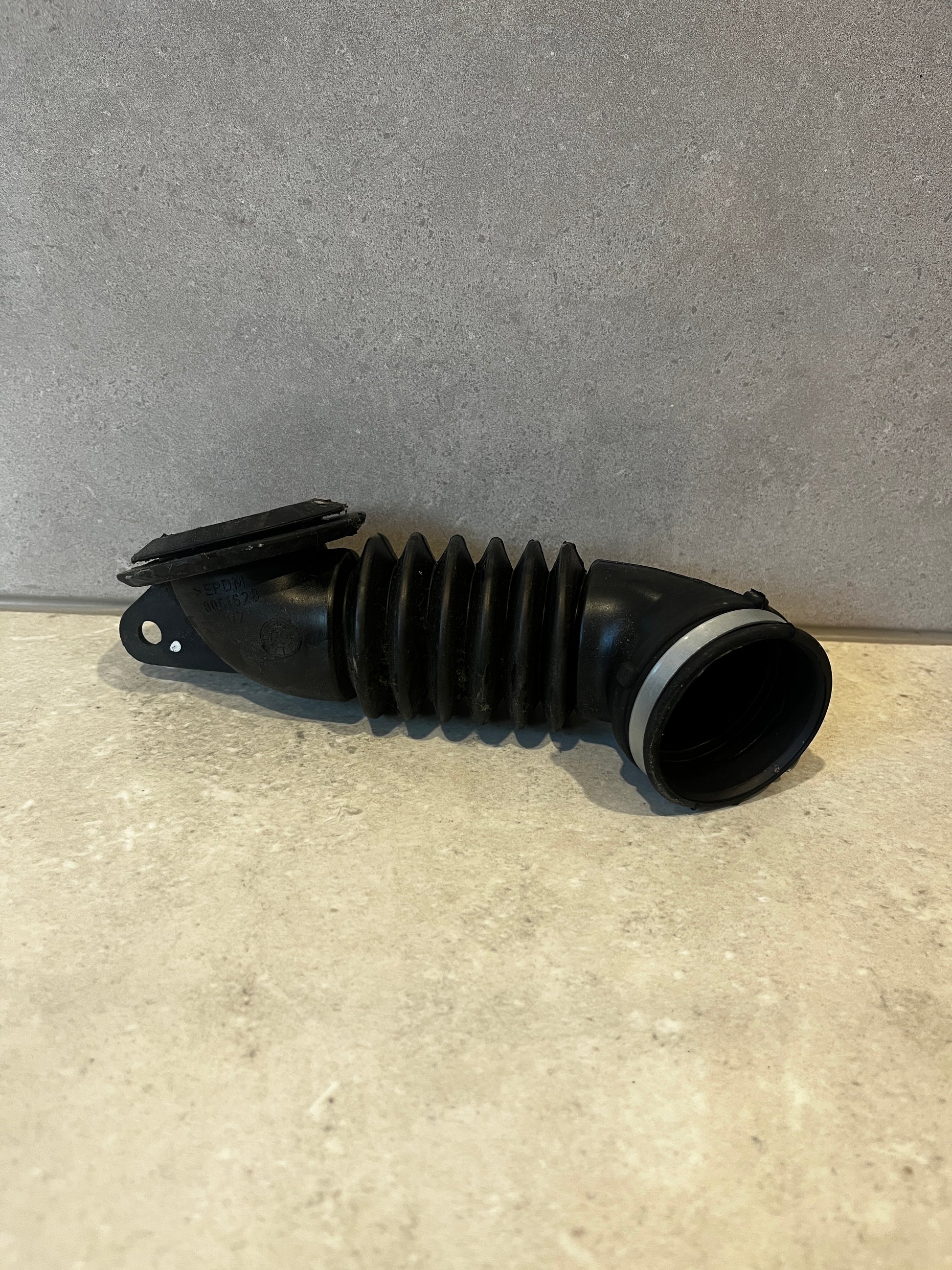 Flexible black EPDM automotive air intake hose on a neutral surface