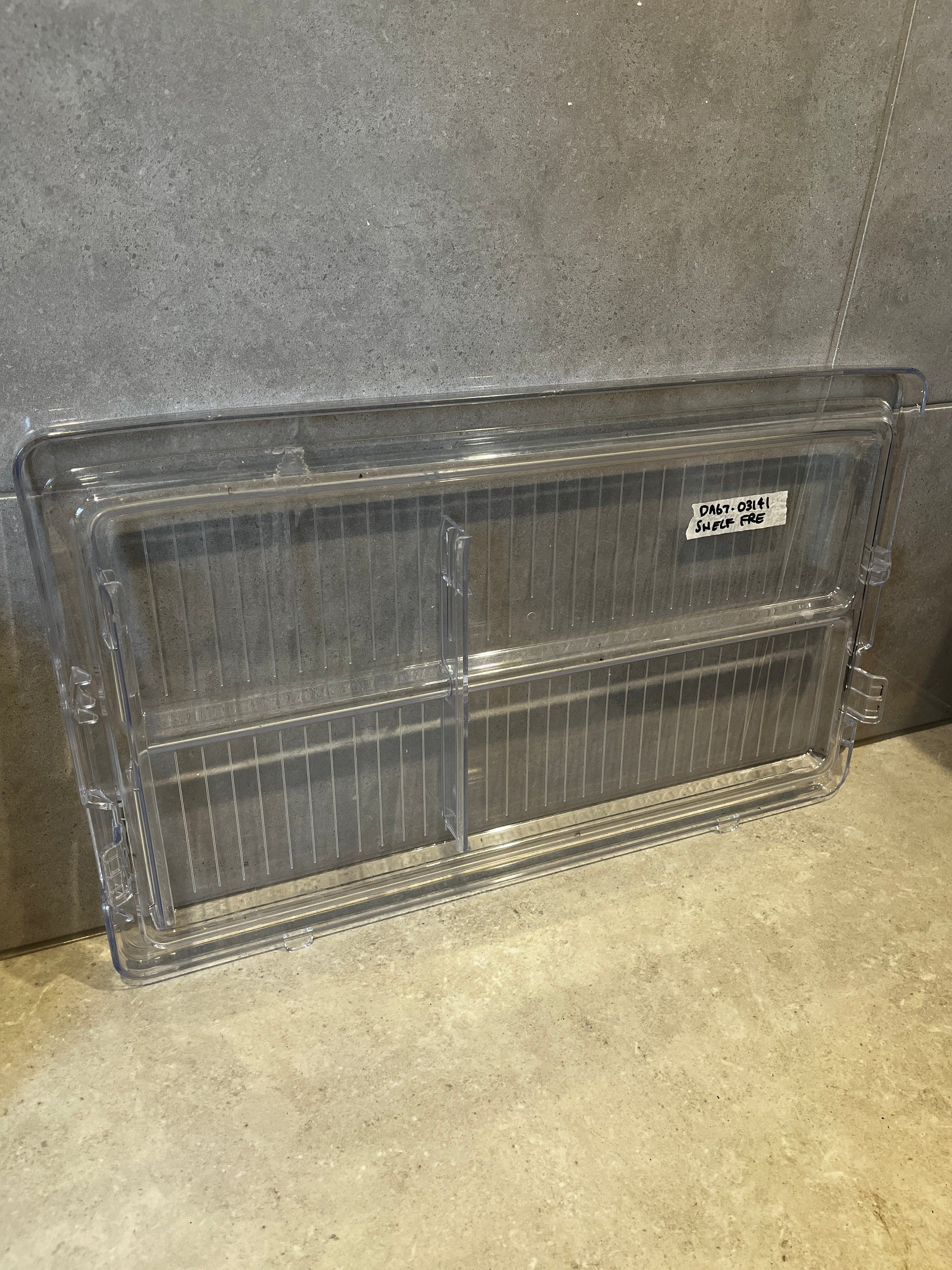 Clear plastic refrigerator shelf bin with dividers on tiled background