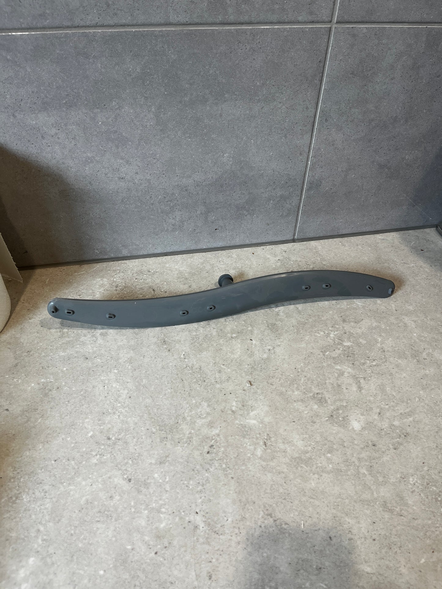 Gray dishwasher lower spray arm on a tiled surface