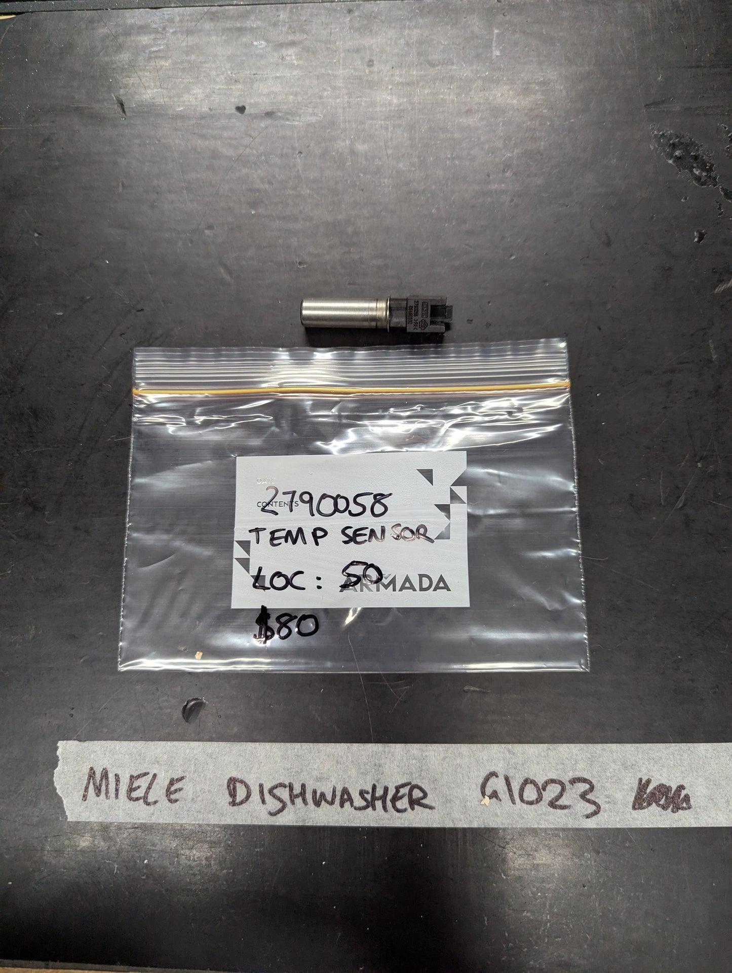 Miele Dishwasher G1023 temperature sensor with labeled bag on black surface