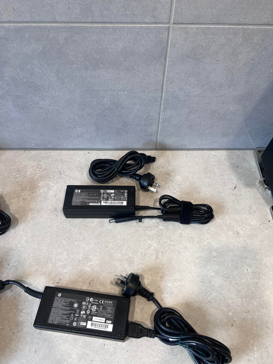 Multiple HP 120W laptop power adapters with power cords on a countertop