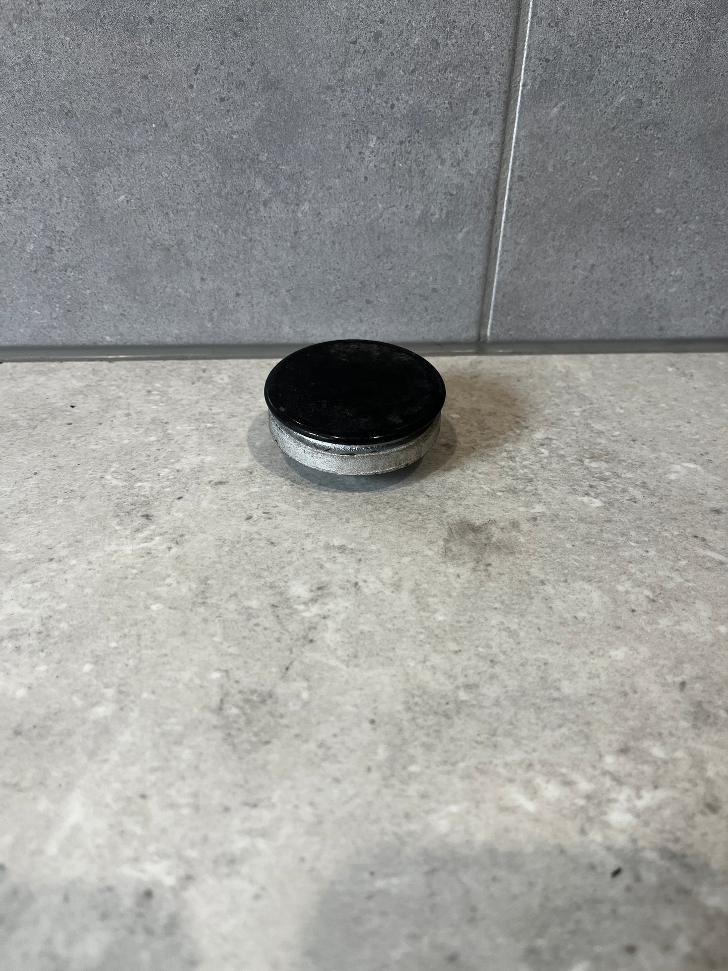 Round metal furniture glide with black protective cap on a stone surface