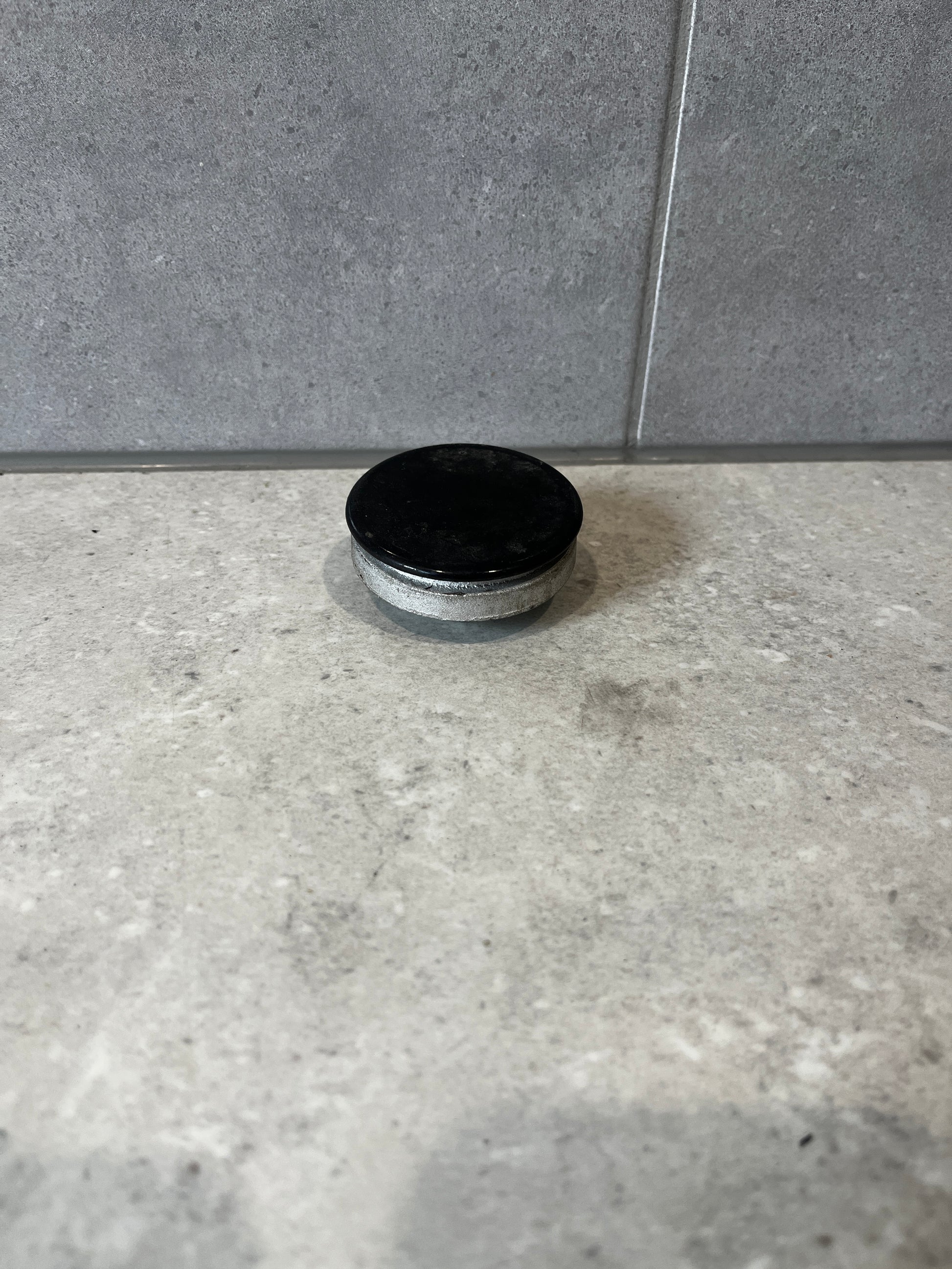 Round metal furniture glide with black protective cap on a stone surface