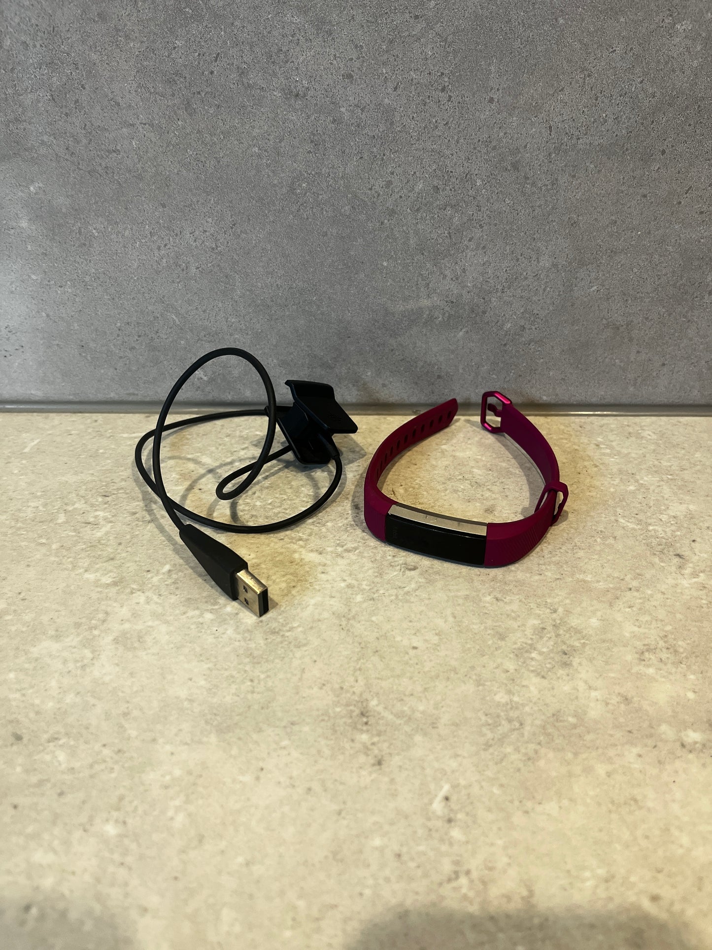 Smart fitness tracker with magenta band and USB charging cable on a stone surface