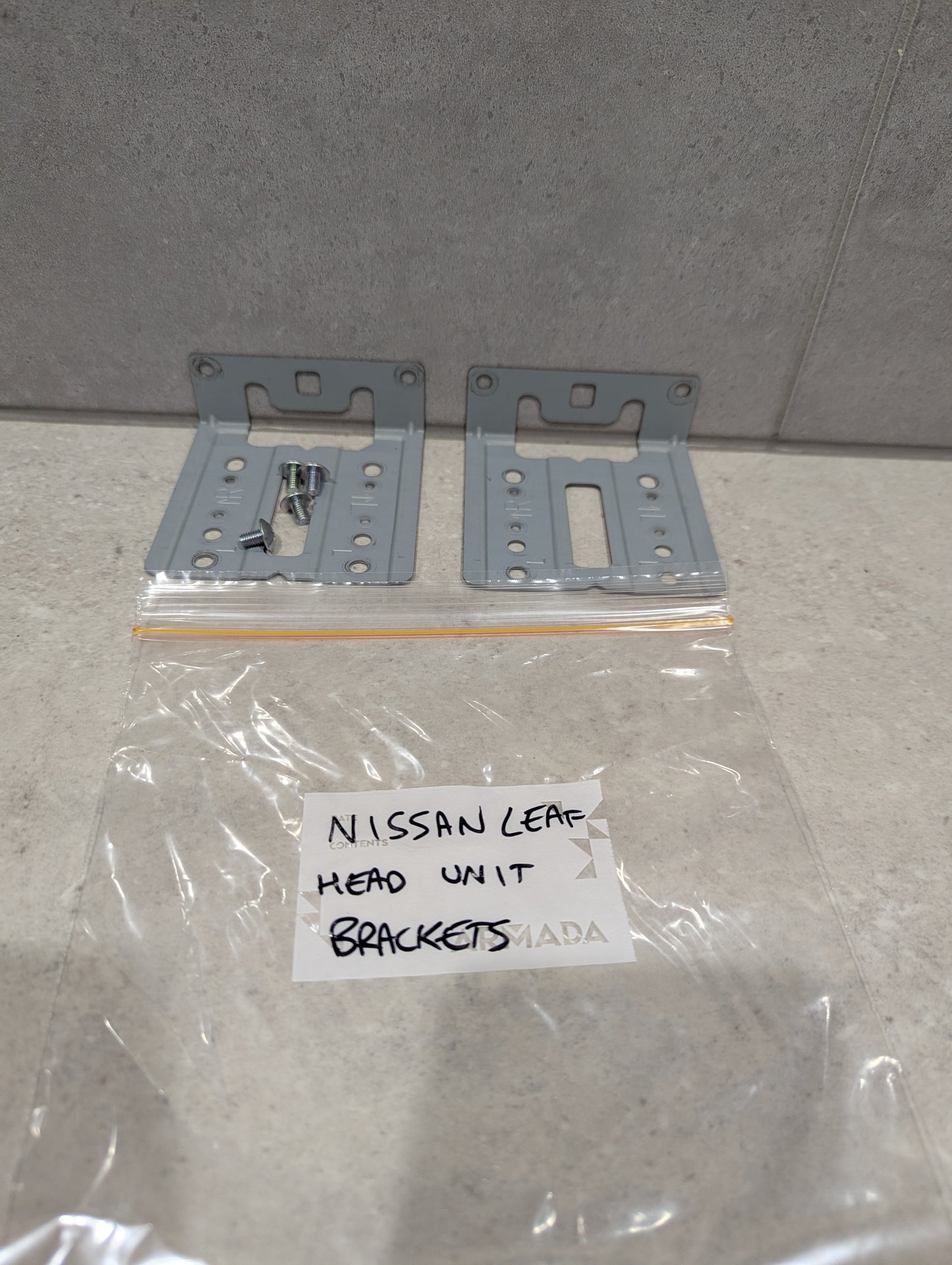 Set of Nissan Leaf head unit mounting brackets with screws and labeled plastic bag