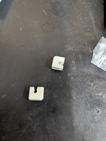 Two plastic top basket pivot clips for a dishwasher on a dark surface
