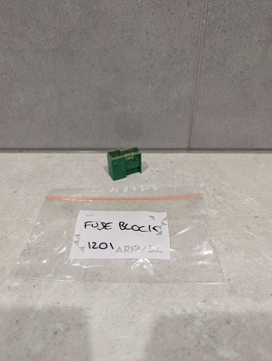 Green plastic fuse block module on a light surface next to a labeled plastic bag