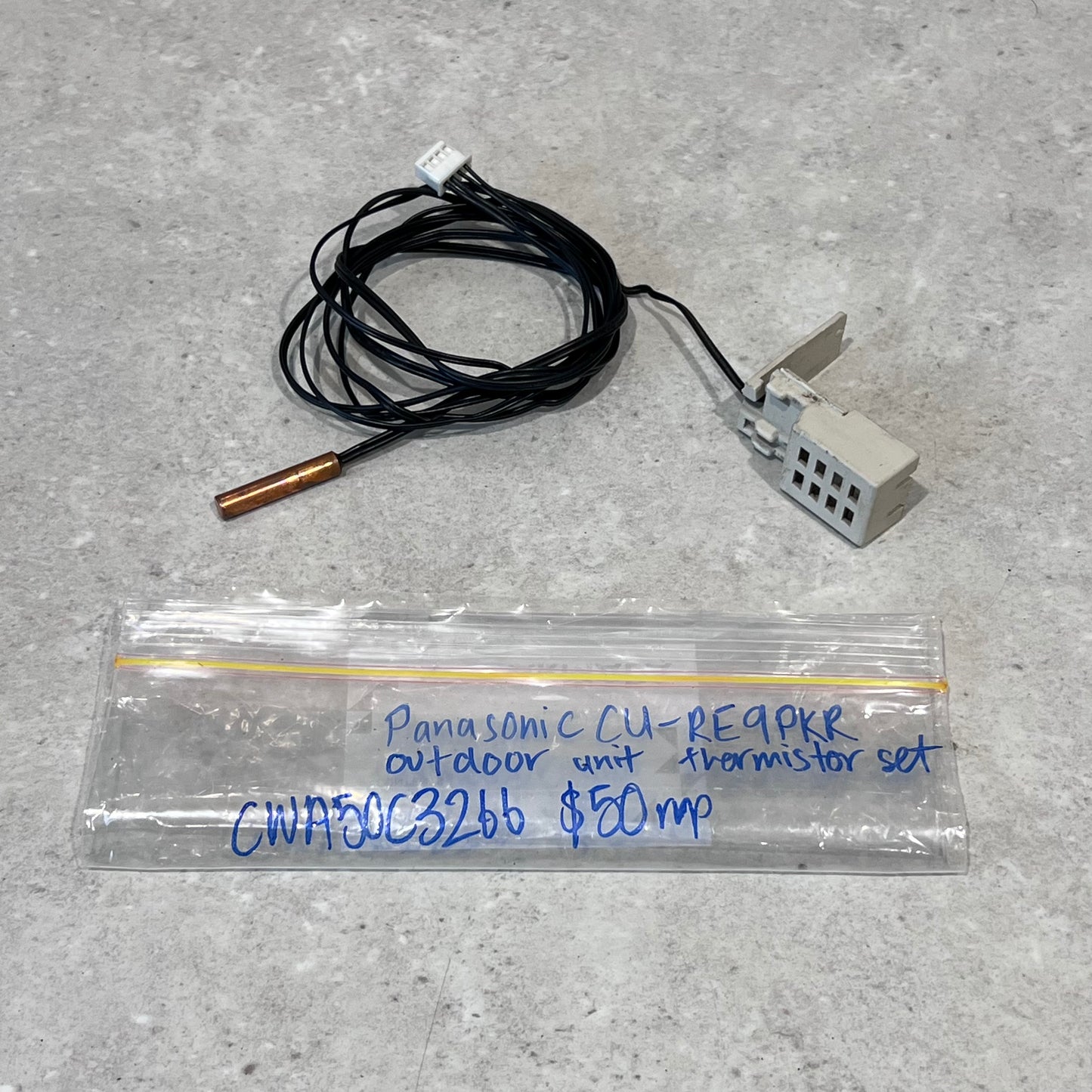 Panasonic CU-RE9PKR outdoor unit thermistor set with wires, copper probe, and sensor module on gray surface