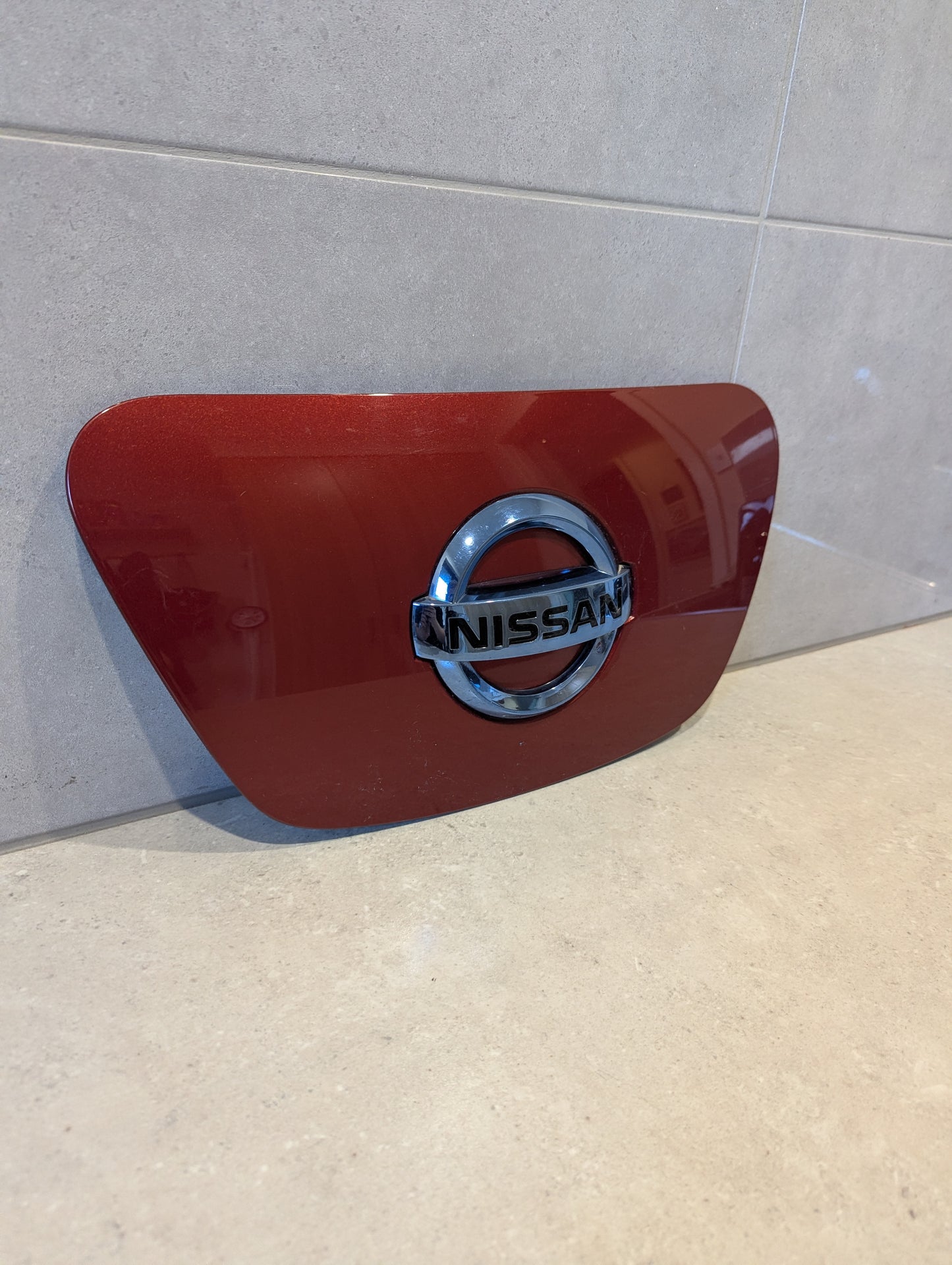 Front view of red Nissan Leaf ZE1 charge port cover with chrome emblem
