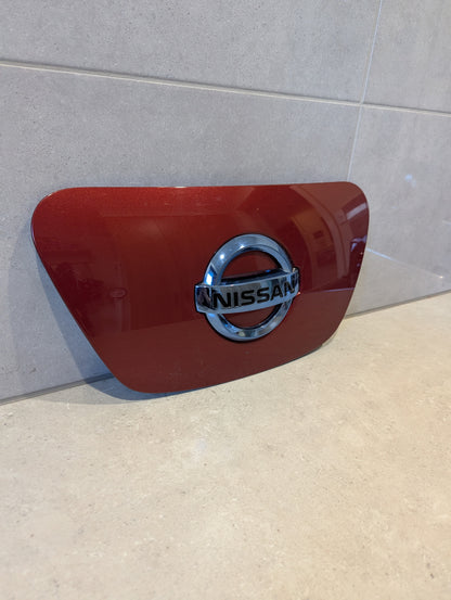 Front view of red Nissan Leaf ZE1 charge port cover with chrome emblem