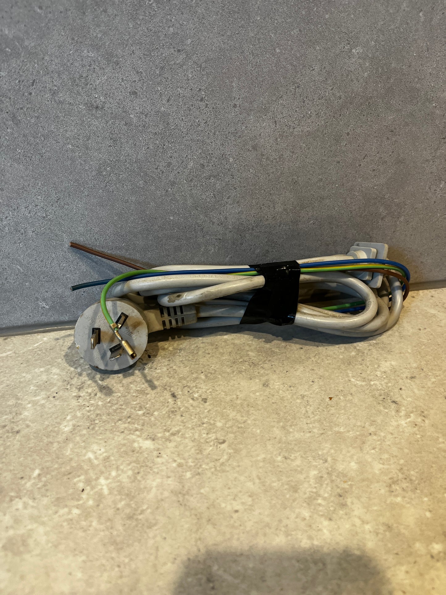 Grounded power cord with three-prong plug and exposed color-coded wires coiled on a stone surface