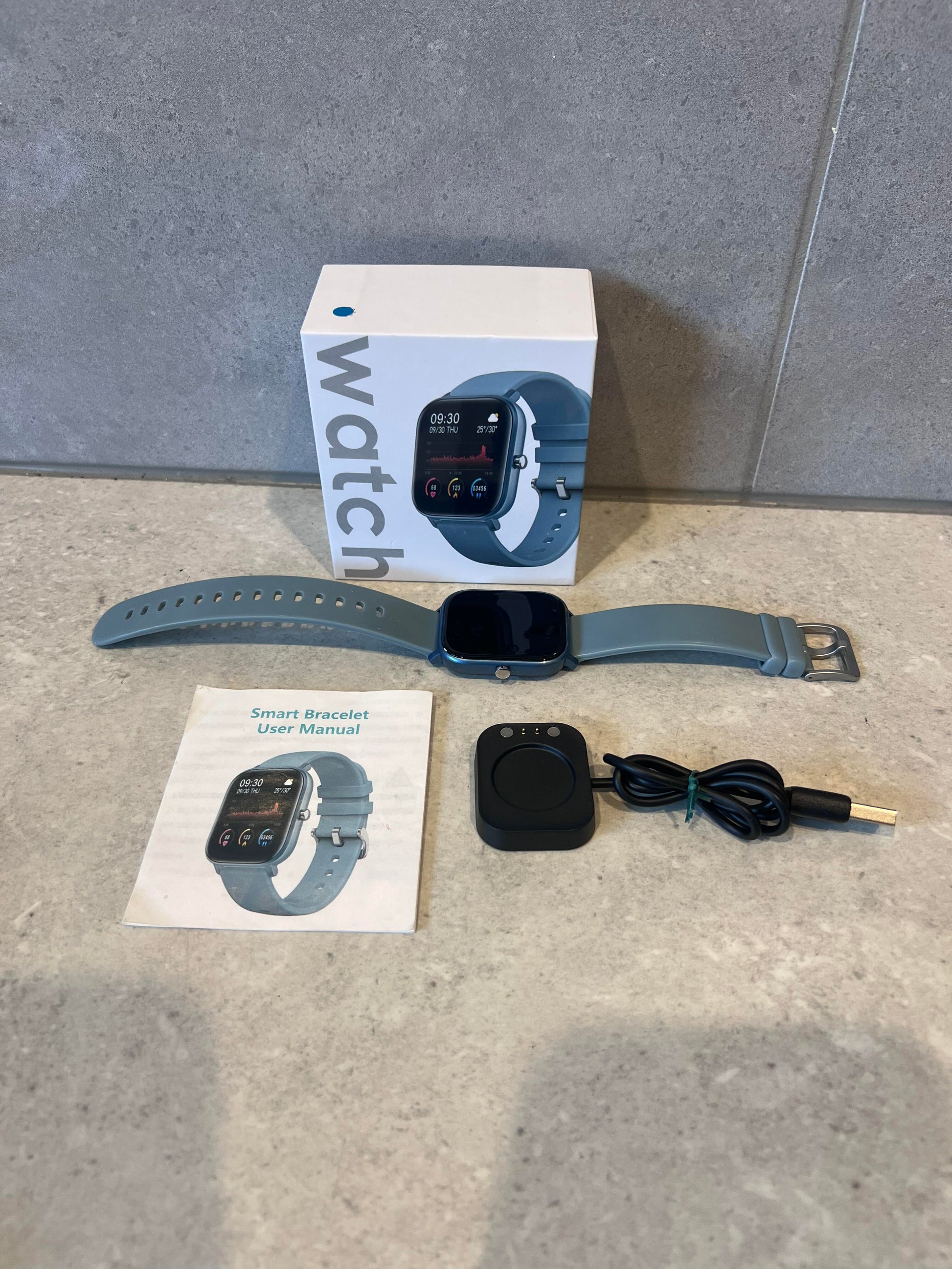 Complete smart watch set with blue strap, box, user manual, charging base, and USB cable