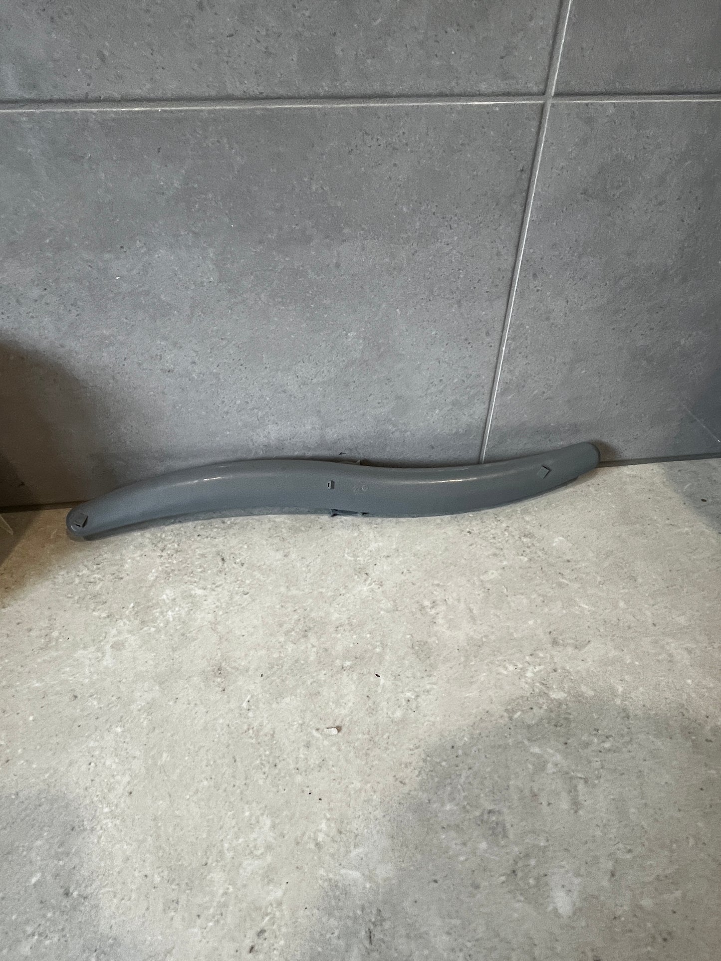 Curved grey plastic part on tiled surface