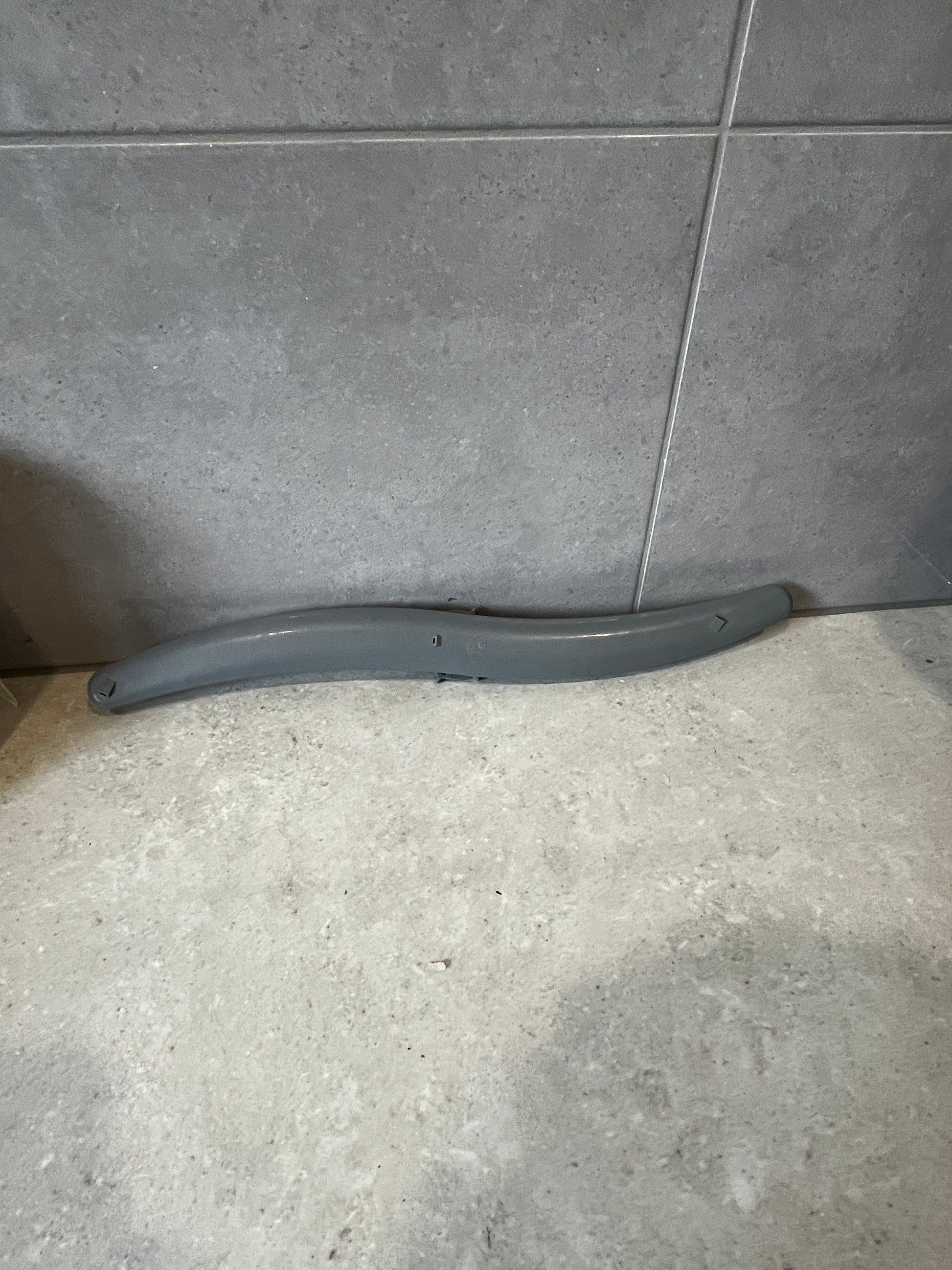 Curved grey plastic part on tiled surface