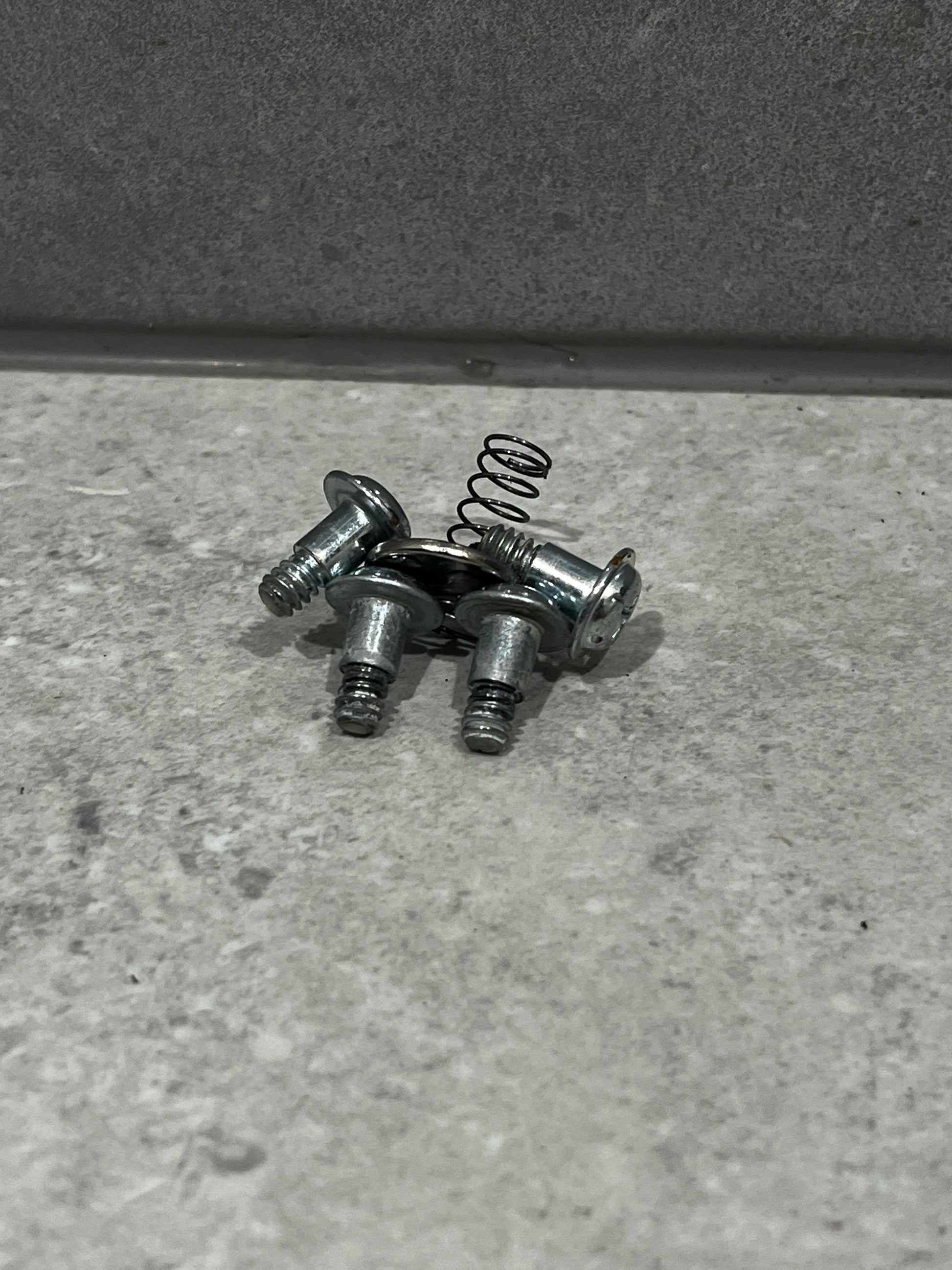 Set of metal screws and small coil spring on gray surface