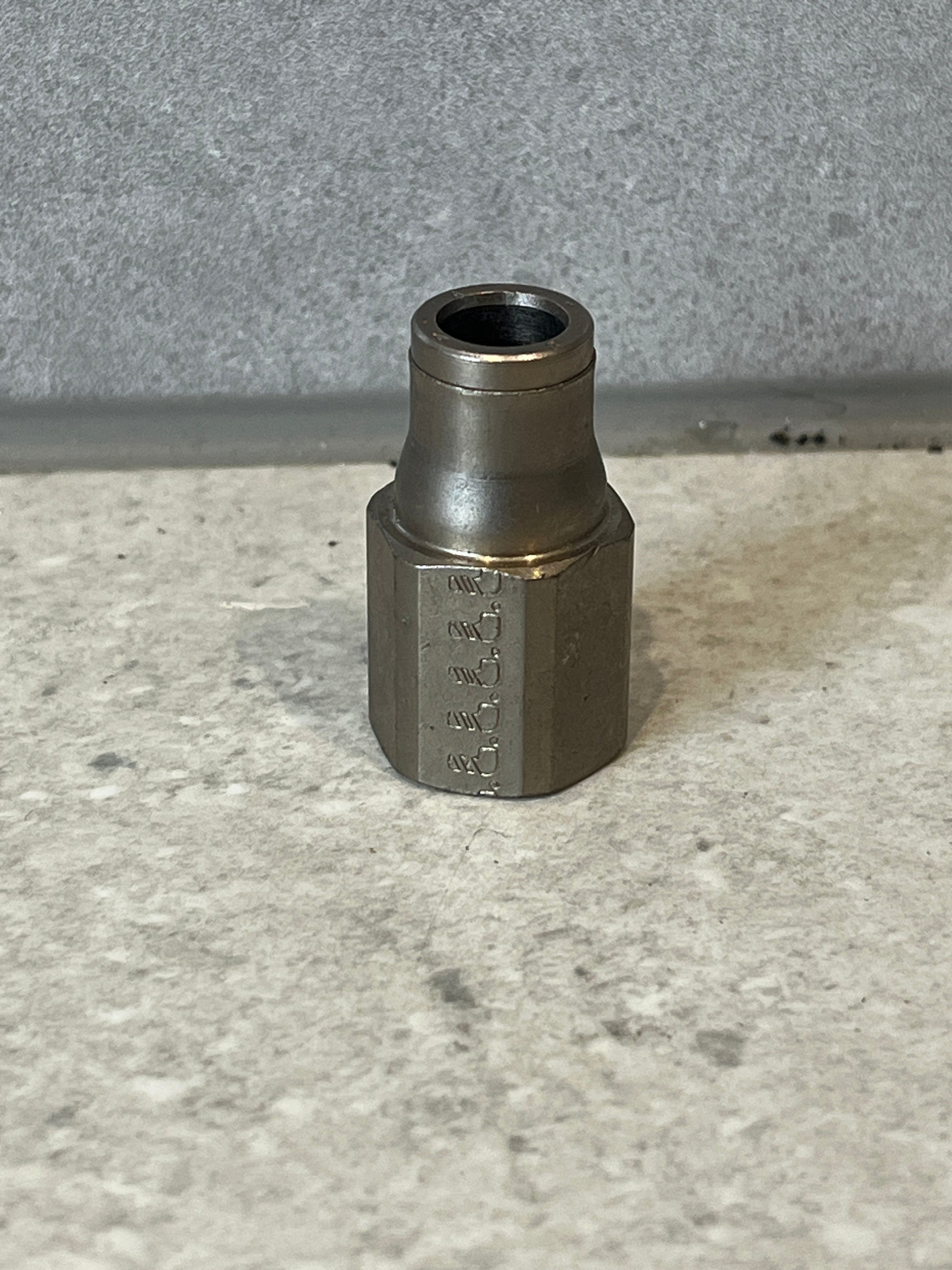 Steel hex hose fitting standing on a gray surface