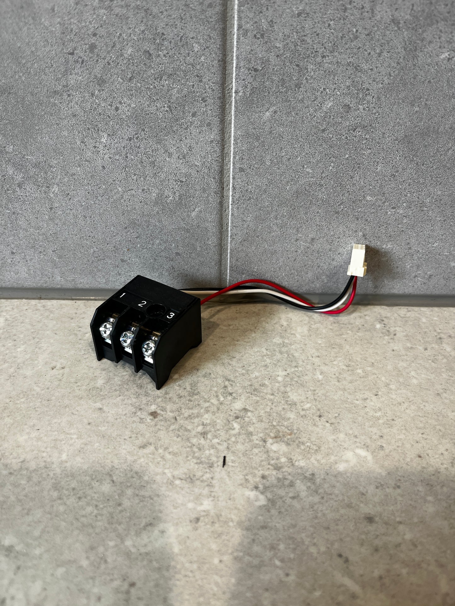 Three-wire terminal block connector with black housing and attached wires on a gray background