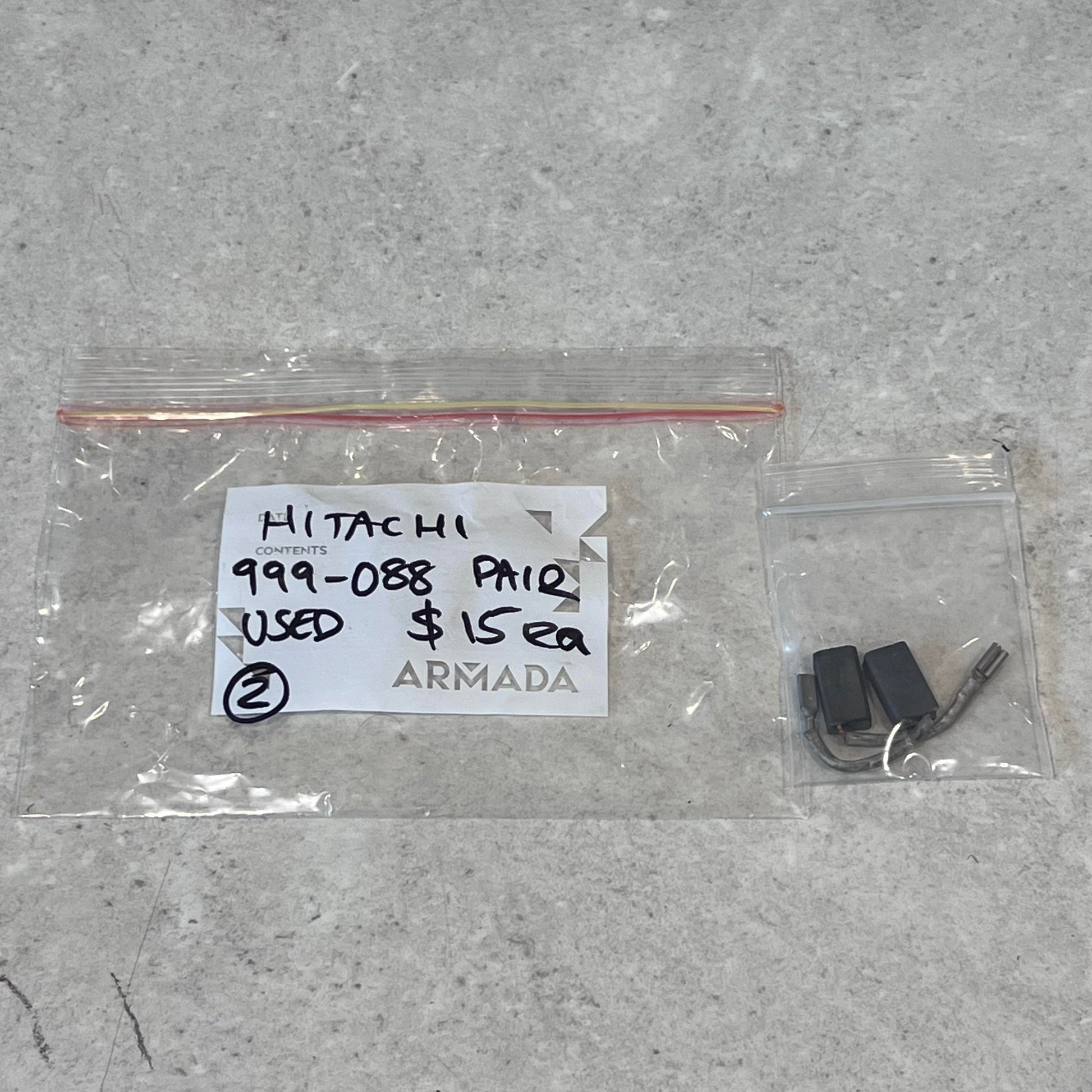 Used Hitachi 999-088 carbon brush pair with connectors in clear bags on a light surface