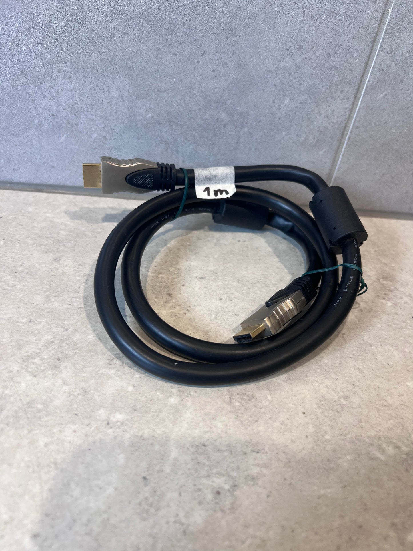 Coiled 1 meter black HDMI cable with gold-plated connectors on a light surface