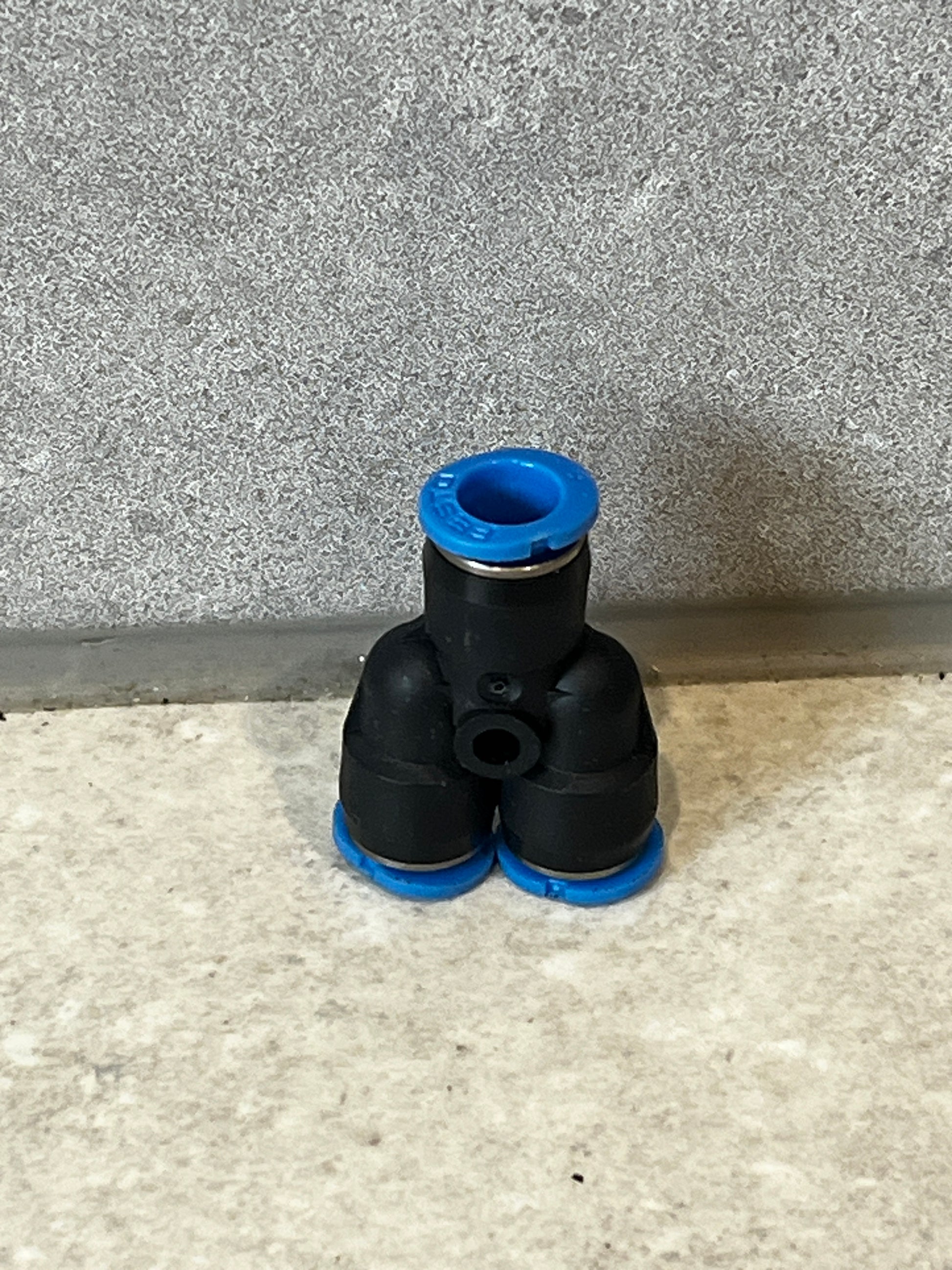 Push-to-connect pneumatic Y fitting with black polymer body and blue ring accents sitting on a tiled surface