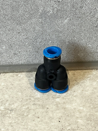 Push-to-connect pneumatic Y fitting with black polymer body and blue ring accents sitting on a tiled surface
