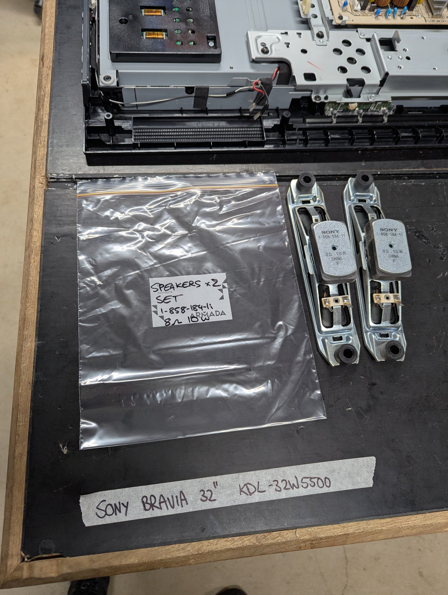 Pair of Sony Bravia KDL-32W5500 TV speakers with metal frames and product label, shown next to TV internal parts