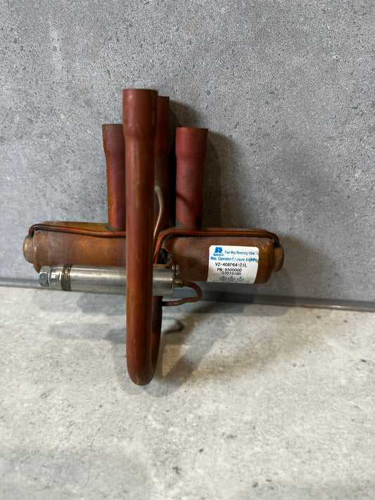 Copper four-way reversing valve on gray background, showing multiple copper tubes and metal housing.