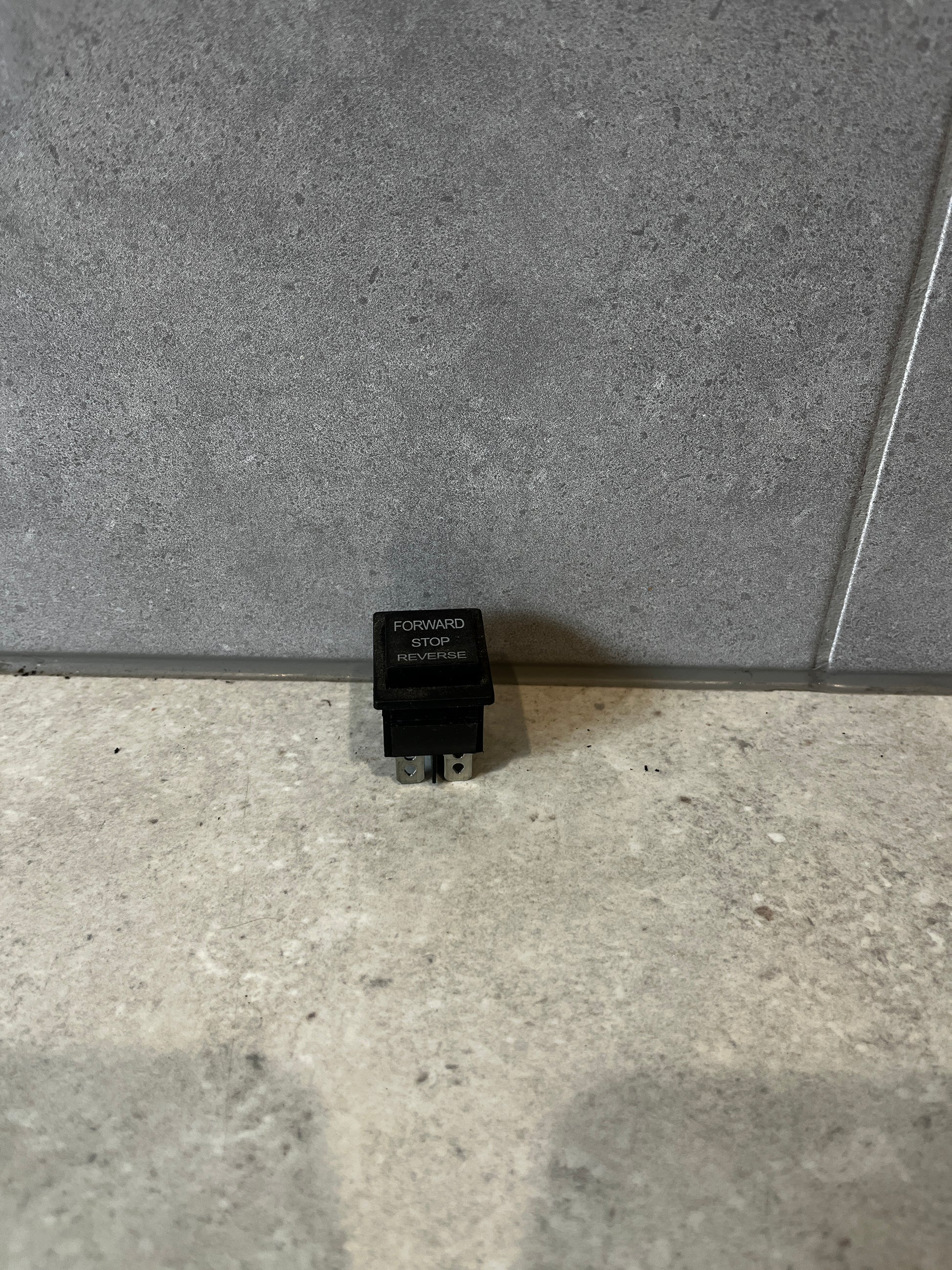 Three-position rocker switch labeled Forward Stop Reverse standing upright on a gray surface
