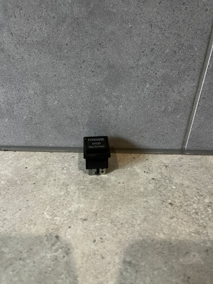 Three-position rocker switch labeled Forward Stop Reverse standing upright on a gray surface