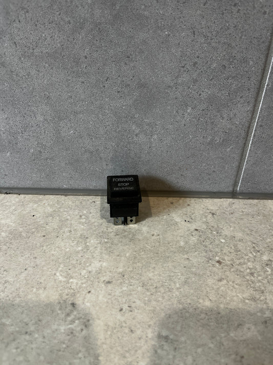 Three-position rocker switch labeled Forward Stop Reverse standing upright on a gray surface