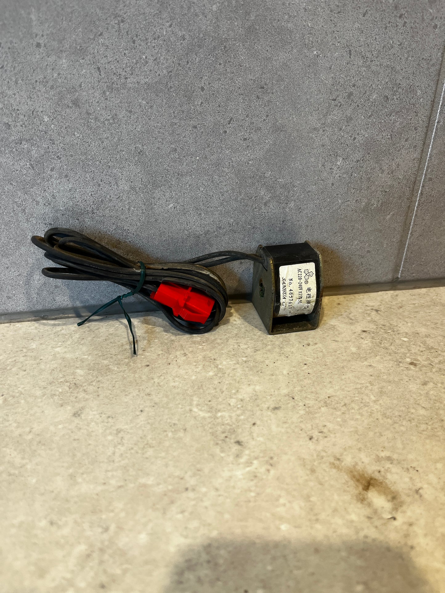 AC 220-240V electrical coil transformer with attached black cable and red connector on gray background