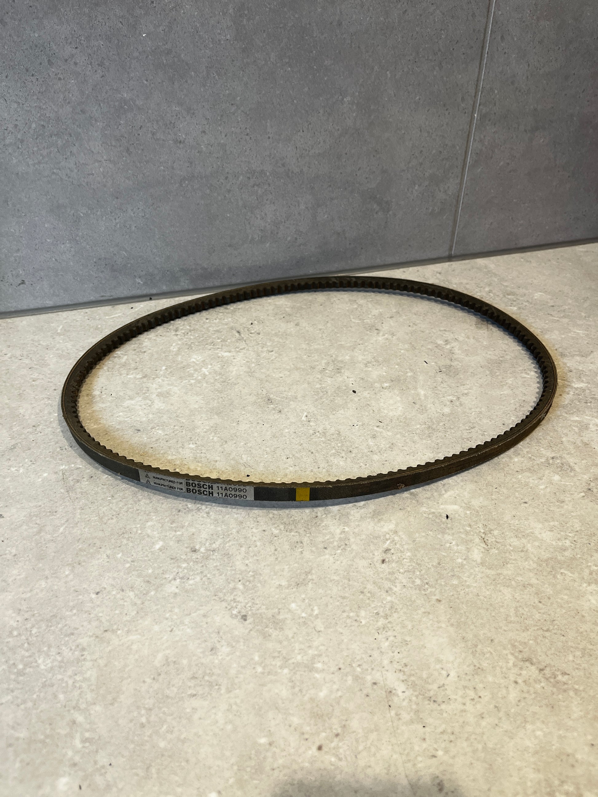 Bosch Drive Belt 11A0990 displayed on a light stone surface