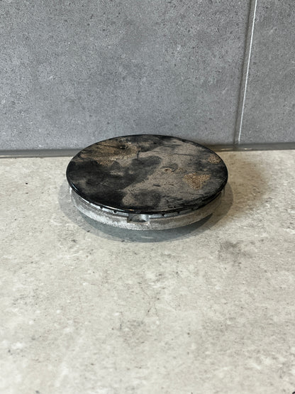 Round metal access cover plate with dark top on concrete surface