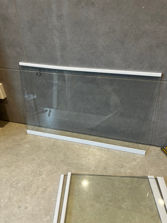 Clear glass panel with white top and bottom frame placed vertically against a tiled wall