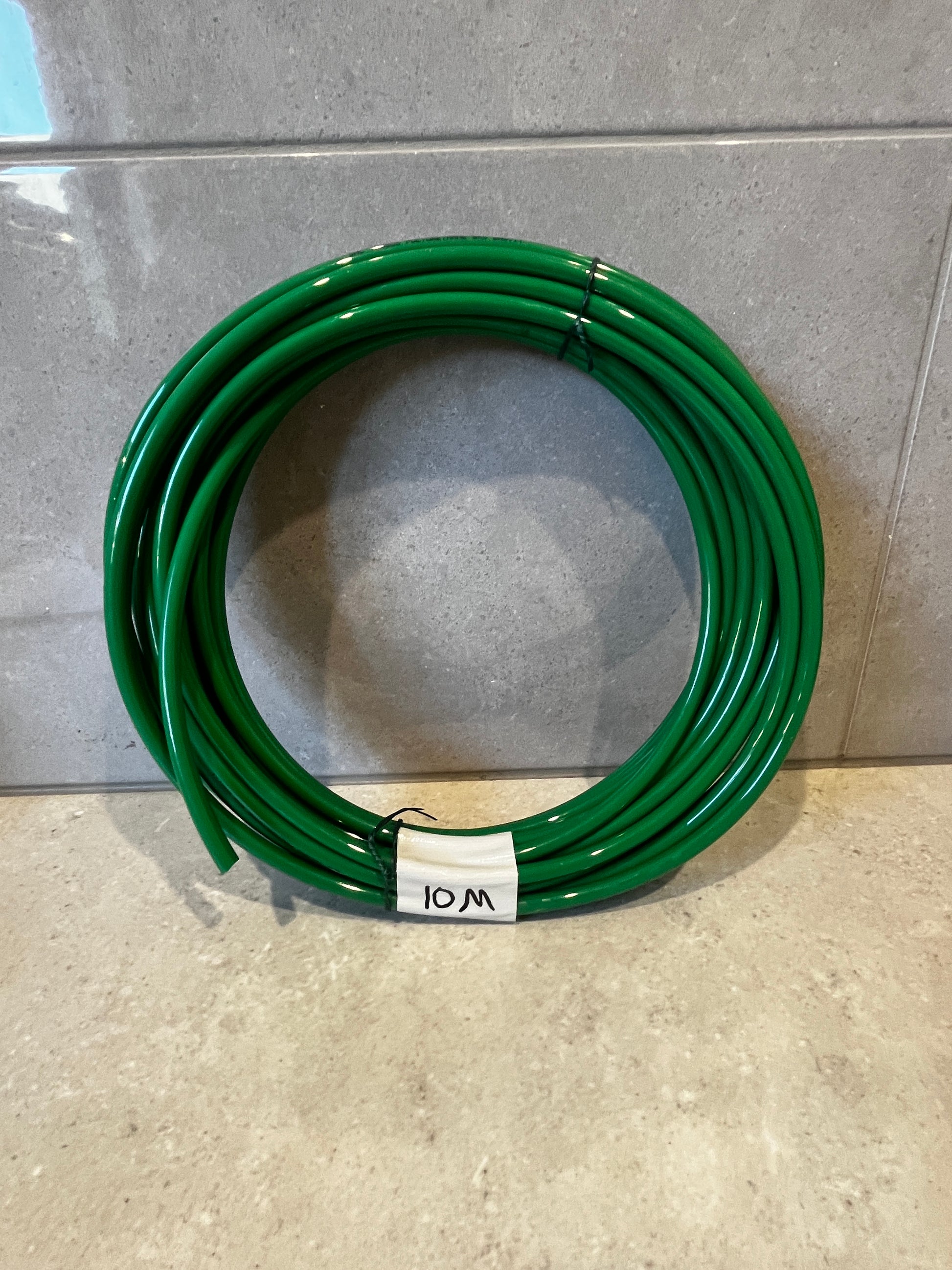 Coiled green polyurethane tubing coil labeled 10M on tiled surface
