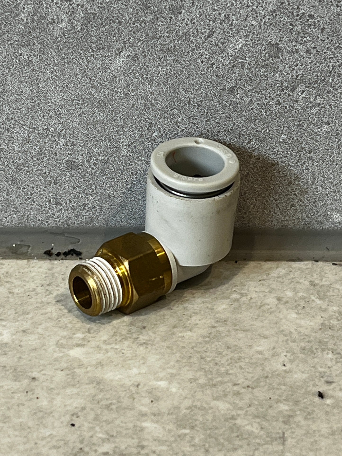 Brass and plastic push-to-connect elbow fitting on gray surface