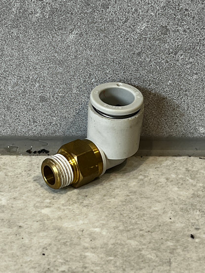 Brass and plastic push-to-connect elbow fitting on gray surface