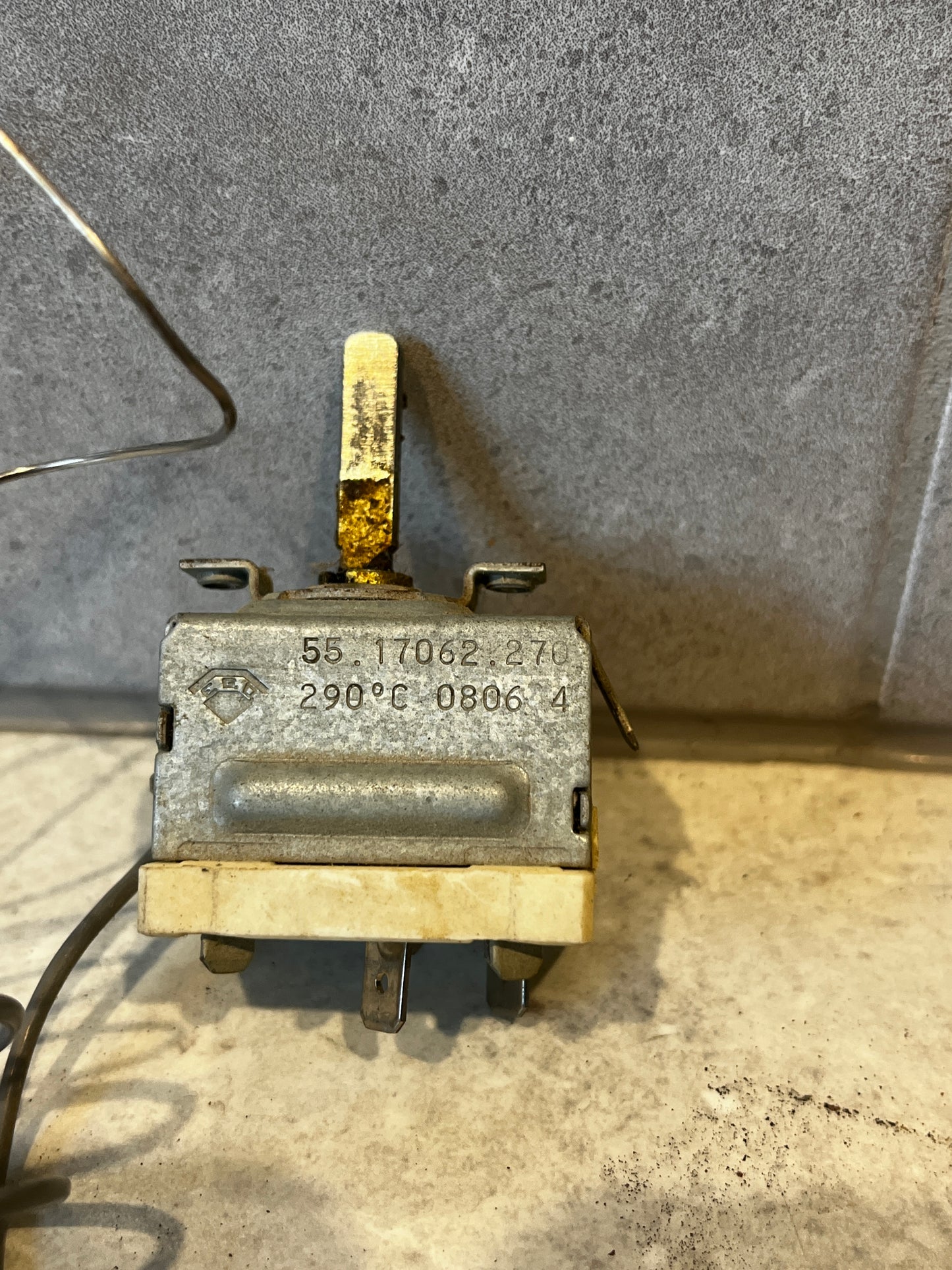 Close-up view of a temperature control thermostat switch with a metal lever and marked 290°C on metal casing