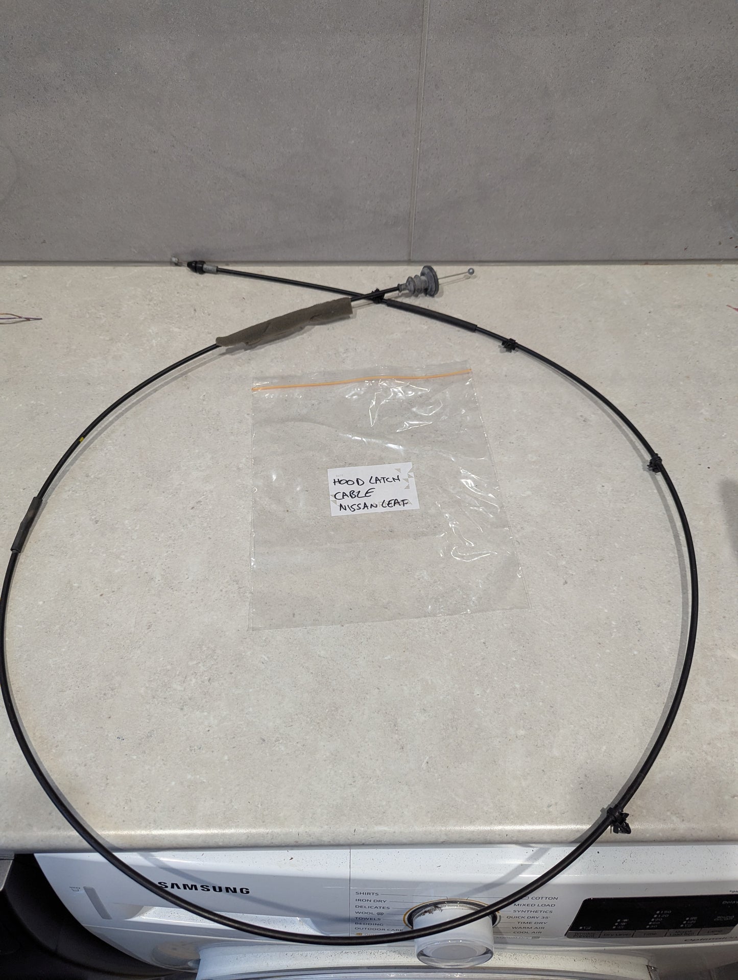 Replacement hood latch cable for Nissan Leaf vehicle displayed on a counter.