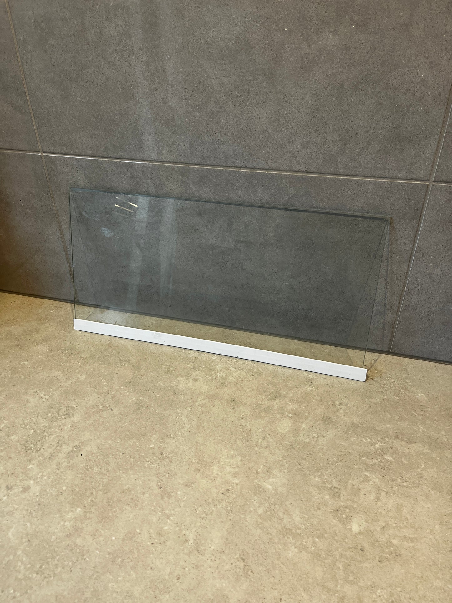 Clear safety glass panel with white base resting on stone surface