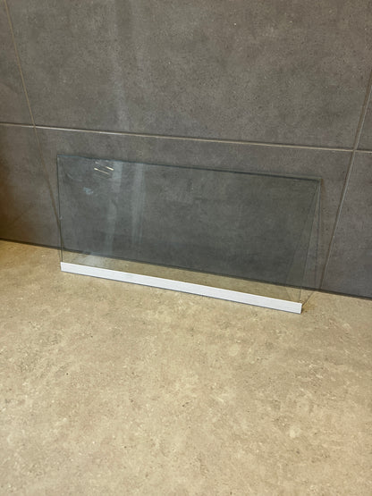 Clear safety glass panel with white base resting on stone surface