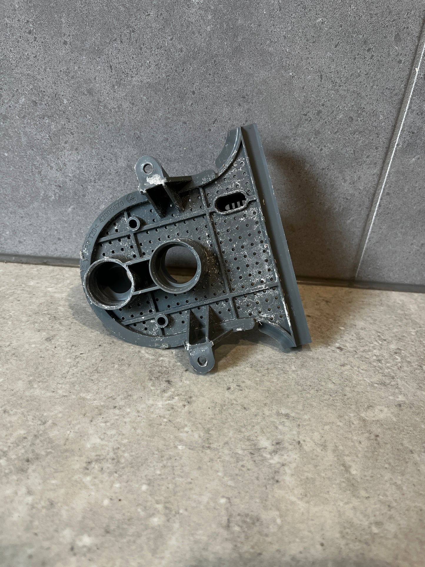 Gray plastic washer pump housing part standing upright on a tile surface