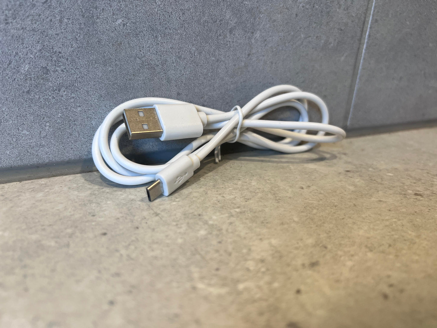 White USB-A to USB-C charging cable coiled on a gray surface