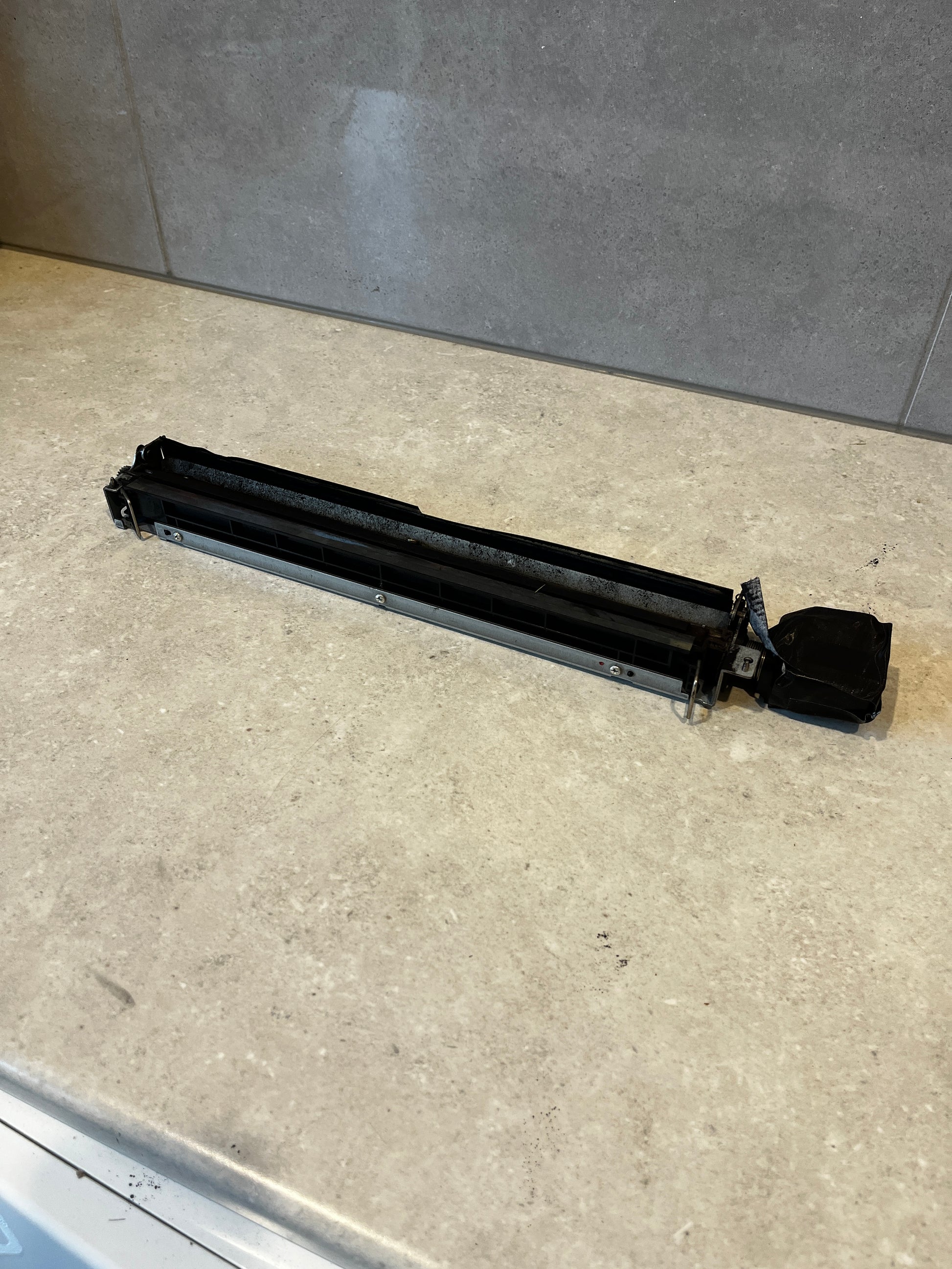 Side view of printer fuser assembly replacement part on countertop