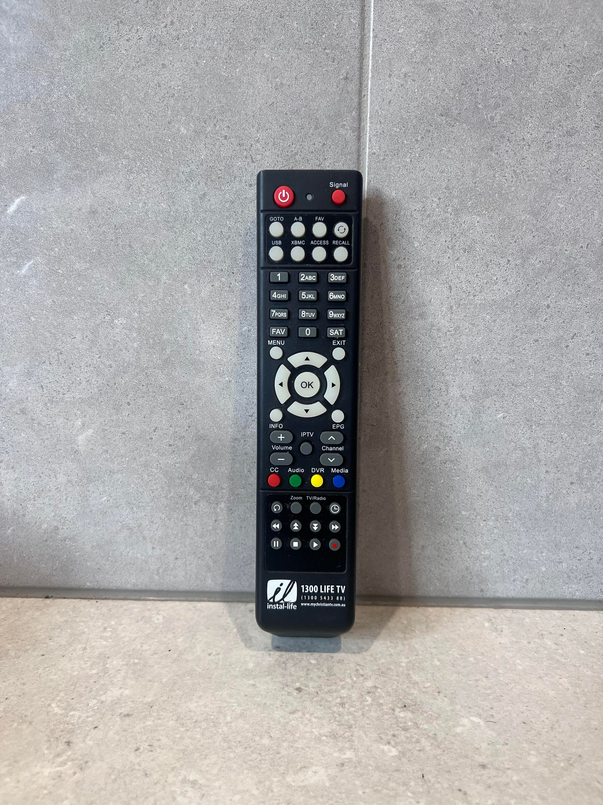 Instal-Life TV universal remote control standing upright against a tiled background
