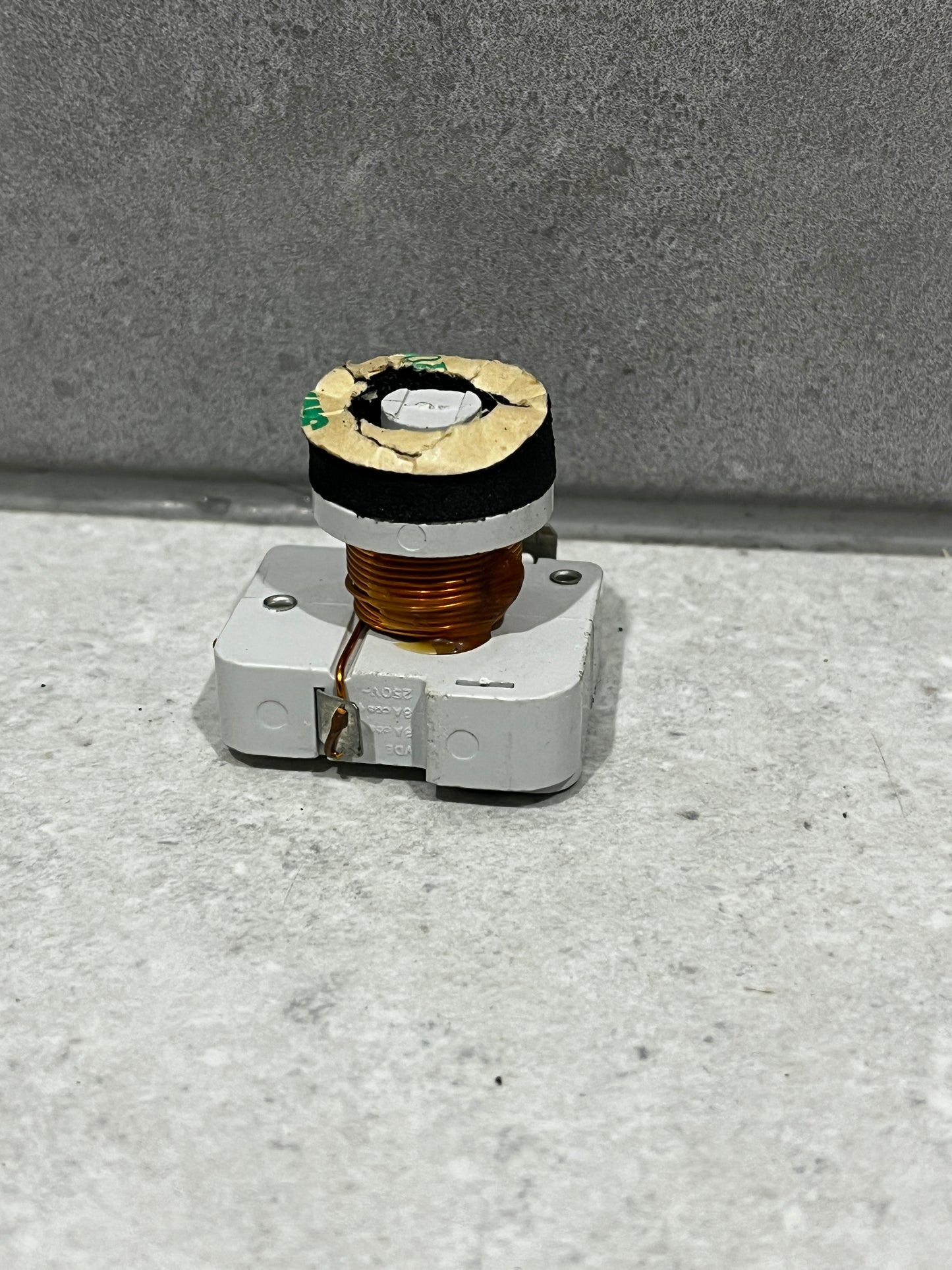 Copper coil component mounted on white plastic base viewed from front